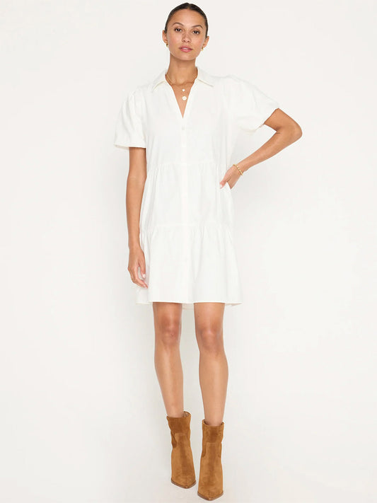 A woman standing in a white Brochu Walker Havana Mini Dress in Ivory and brown suede boots, with her hands on her hips.
