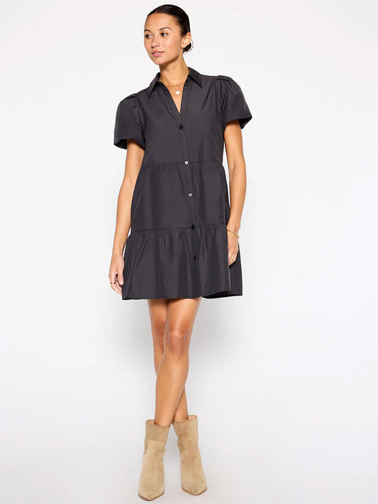 A woman in a Brochu Walker Havana Mini Dress in Washed Black with a tiered skirt and light beige ankle boots stands against a plain background.