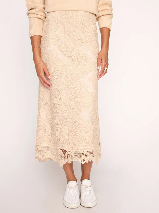 A person wearing a Brochu Walker Mara Lace Skirt in Buff with a scalloped hem and white sneakers.