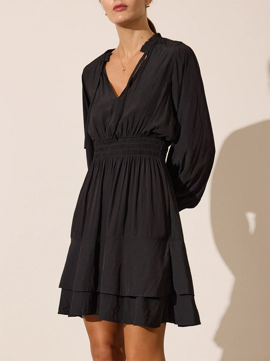 Woman in a black Brochu Walker Olivia Smocked Dress with long sleeves, an elastic waist, and tiered skirt against a neutral background.