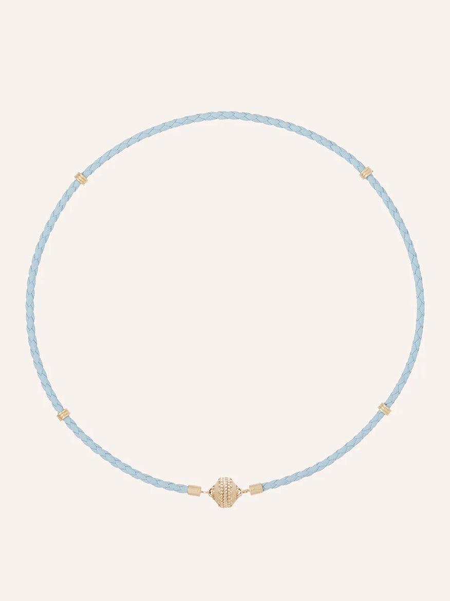 The Clara Williams Aspen Braided Light Blue Leather Mini Necklace features gold-tone bead accents and a central 14K yellow gold decorative bead, shown on a plain background.