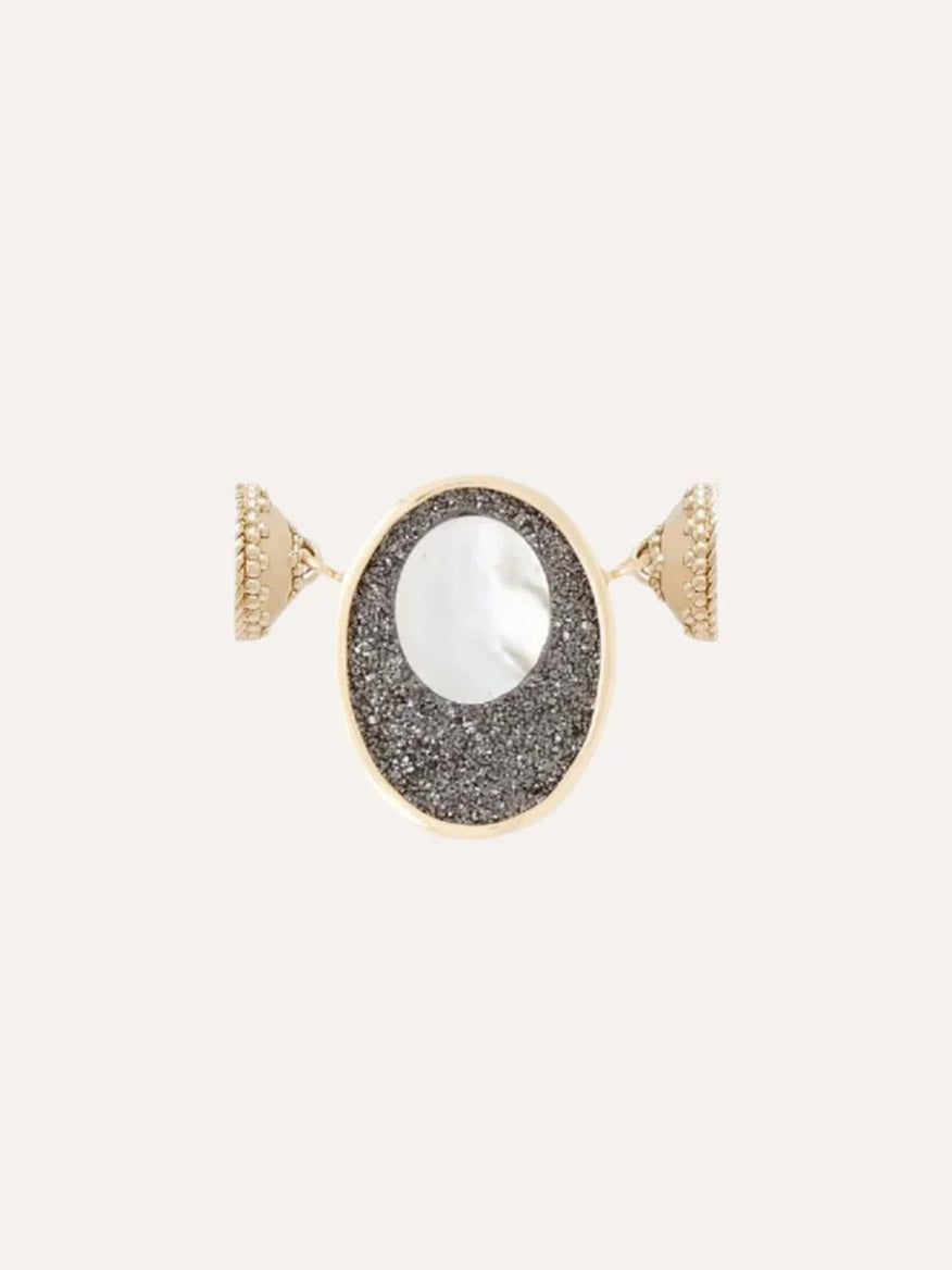 The Clara Williams 14K Black Druzy Oval Cut-Out Mini Centerpiece features an oval face with a white circular center set on a textured black druzy background, all elegantly crafted in 14K yellow gold.