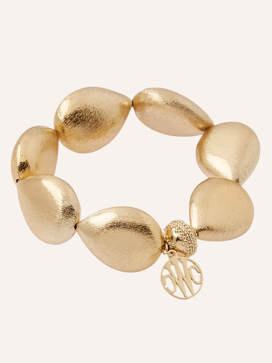 The Clara Williams Gold Rush Large Teardrop Stretch Bracelet features large gold-toned textured teardrop beads, a signature ClaraClasp bead, and a round monogram charm for elegant style.