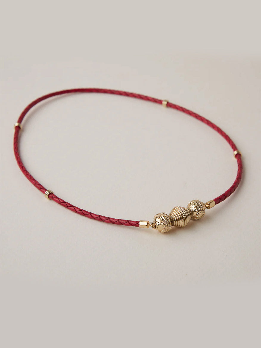 The Clara Williams Gold Lantern Mini Centerpiece is a thin red braided necklace featuring 14K gold plated center beads and lantern bead accents, shown on a neutral background.