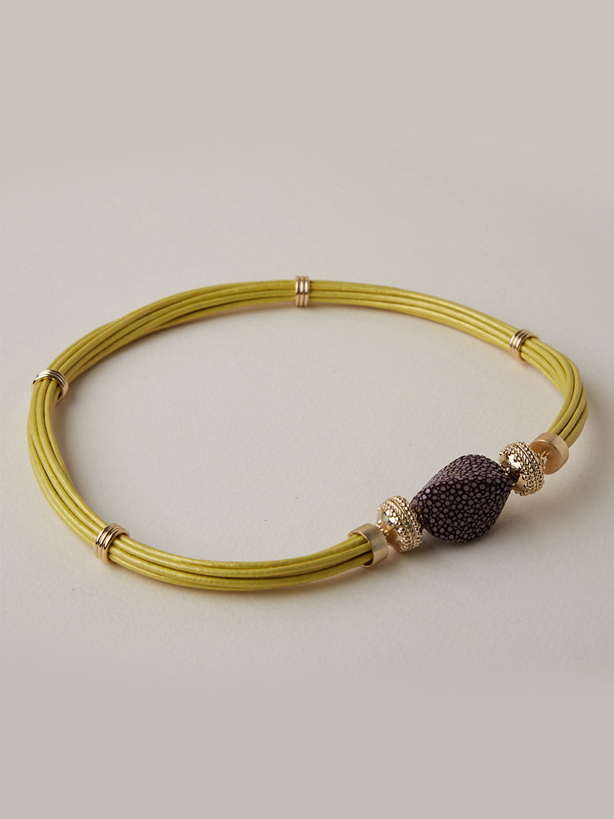 Clara Williams Small Plum Stingray Centerpiece: A yellow multi-strand necklace adorned with 14K yellow gold rings and a central bead featuring a luxurious plum-colored stingray texture, displayed on a light background.