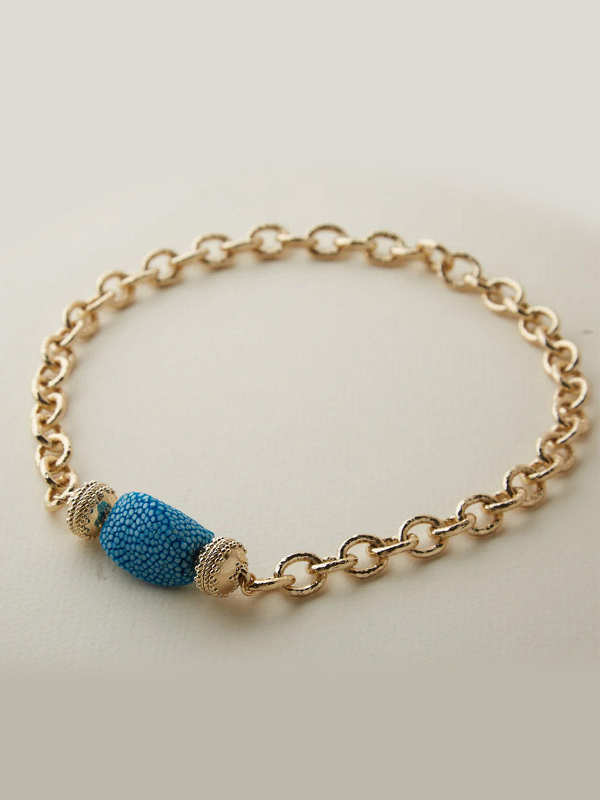 The Clara Williams Wabash Necklace features hammered oval links and a textured blue bead centerpiece with decorative gold caps, all crafted in 14K yellow gold and showcased on a light background.