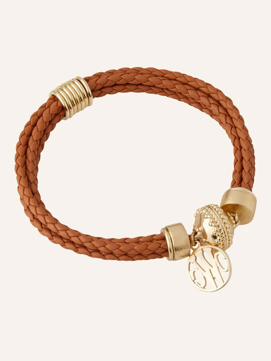 The Clara Williams Wellington Braided Leather Brown Bracelet features a brown braided leather band, ClaraClasp, and a round 14K yellow gold charm with engraved initials for personalized style.