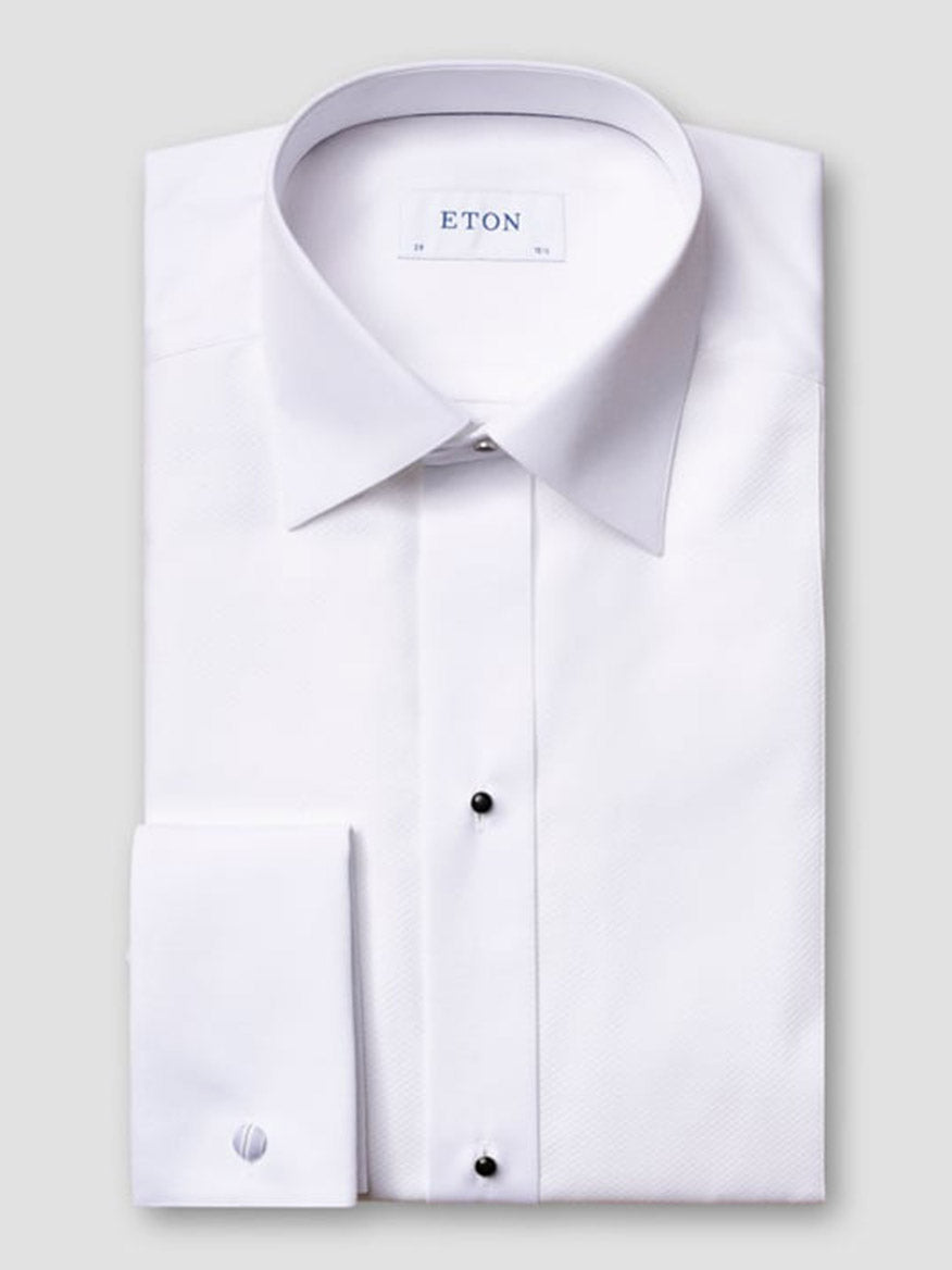 The Eton Slim Fit Piqué Bib-Front White Tie Evening Shirt in White features black buttons and French cuffs, neatly folded against a plain light gray background. The wing collar label displays "ETON.