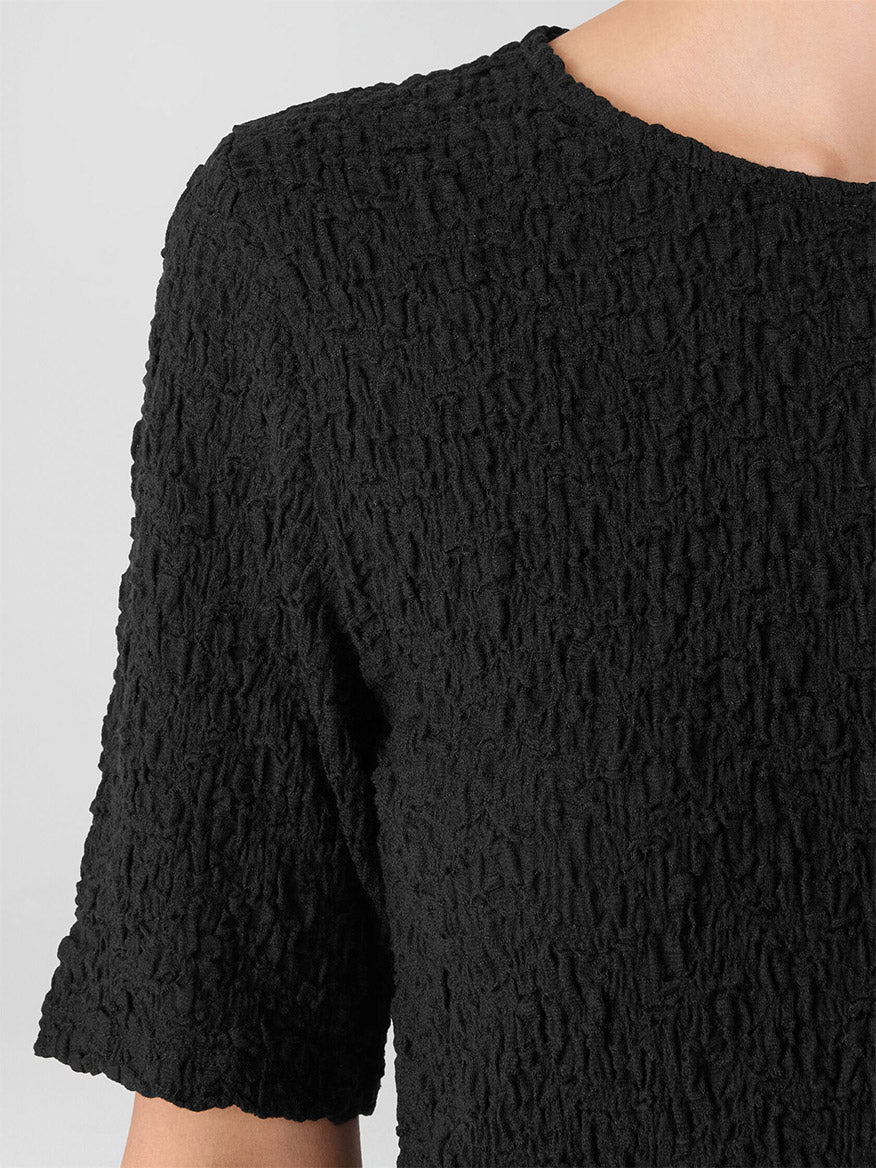 Close-up of a person wearing the Eileen Fisher Bubble Jacquard Crew Neck Top in Black, featuring short sleeves and a textured jacquard finish, shown from the shoulders to the upper chest.