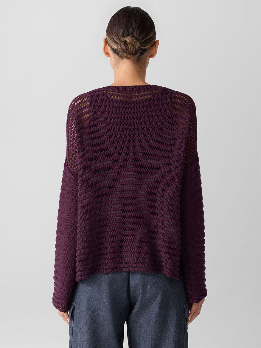 A person with brown hair in a low bun is seen from the back wearing the Eileen Fisher Peruvian Organic Cotton Cord Crew Neck Top in Blackberry, paired with gray pants, against a plain light background.