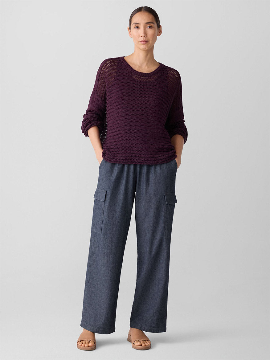 A person stands facing forward, wearing the Eileen Fisher Peruvian Organic Cotton Cord Crew Neck Top in Blackberry, wide-leg gray cargo pants, and tan sandals against a plain light gray background.