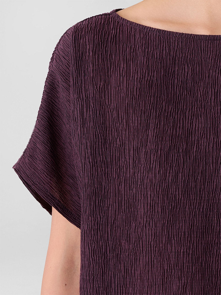 A close-up of a person wearing the Eileen Fisher Woven Plissé Dolman Sleeve Top in Blackberry, featuring short dolman sleeves and a wide neckline.
