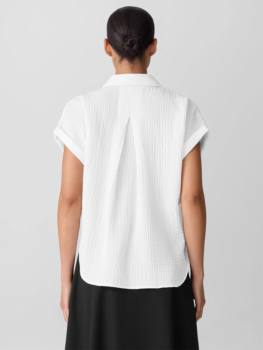 A person stands facing away, wearing the Eileen Fisher Organic Cotton Lofty Gauze Notch Collar Top in White with a black skirt, their hair pulled back neatly.