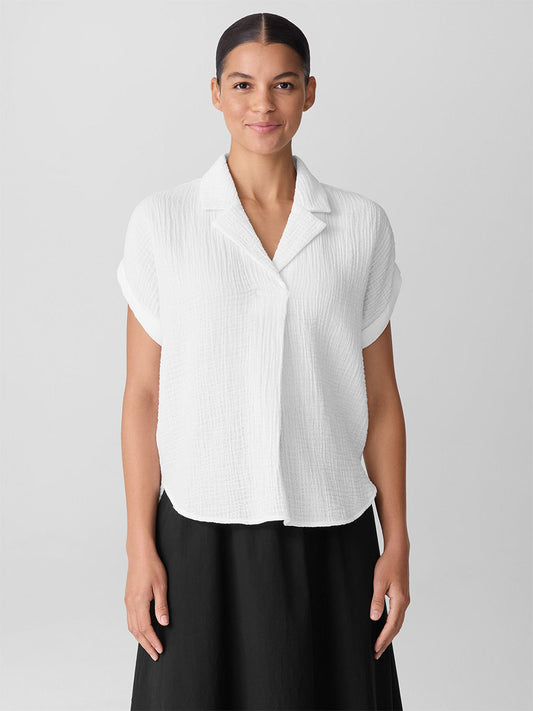 A person stands facing forward, wearing the Eileen Fisher Organic Cotton Lofty Gauze Notch Collar Top in White and a black skirt against a plain light background.