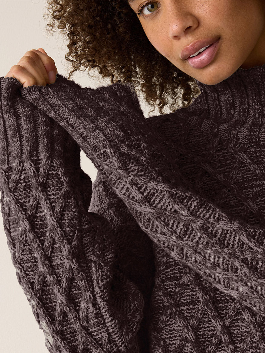A person wearing a dark brown Eileen Fisher Peruvian Cotton Boucle Fluff Turtleneck in Coffee, pulling up one sleeve of the cable-knit sweater.