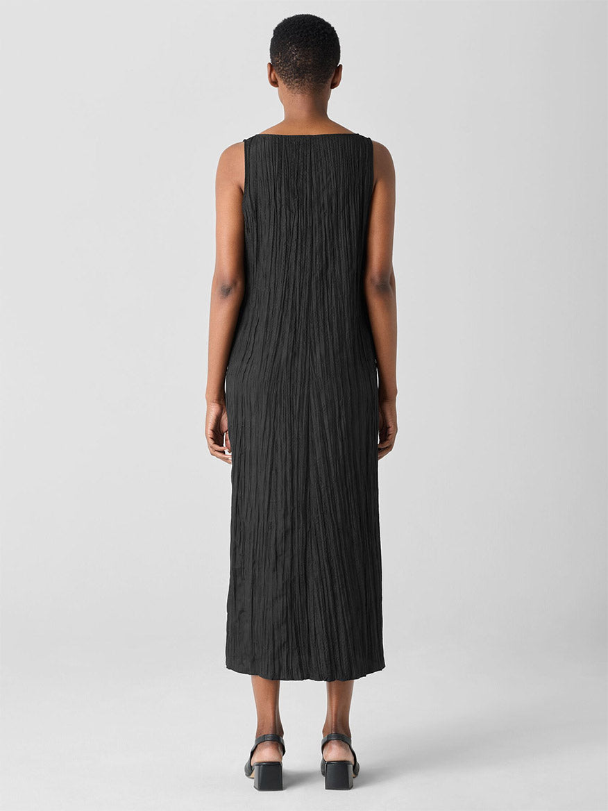 The back view features someone wearing the Eileen Fisher Crushed Silk V-Neck Dress in black, a sleeveless outfit with a crinkled texture, paired with dark sandals against a plain background.