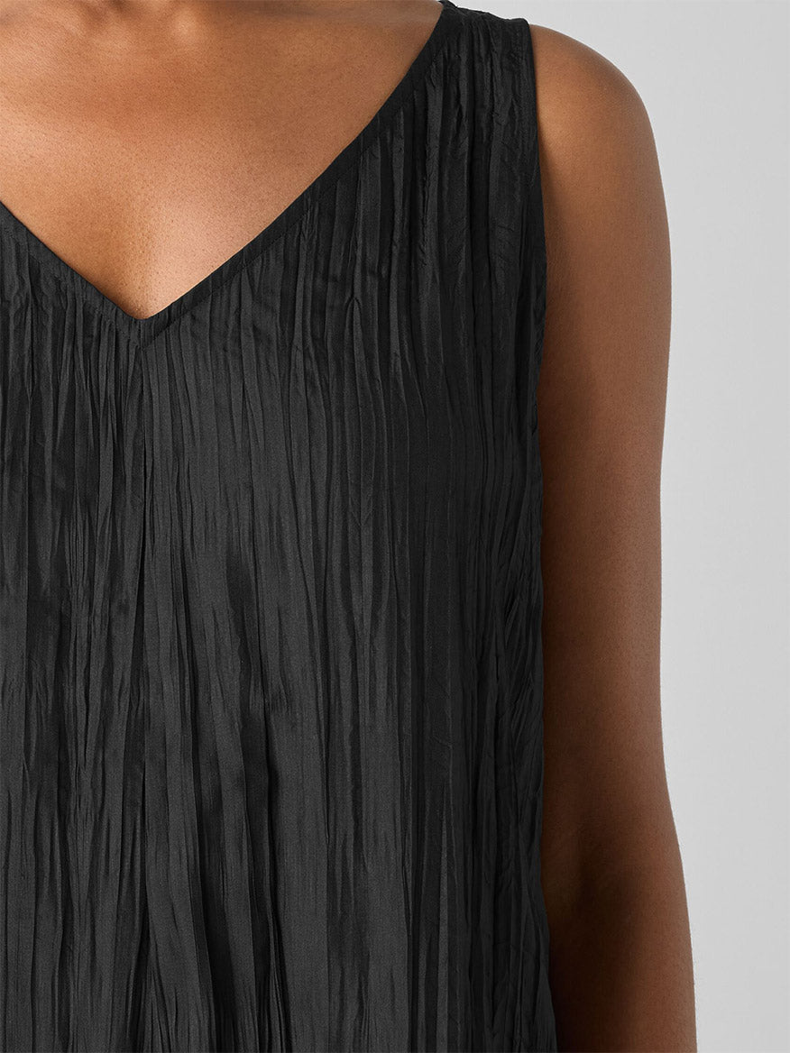 Close-up of a person in the Eileen Fisher Crushed Silk V-Neck Dress, featuring a pleated, crinkled surface, set against a plain gray background.