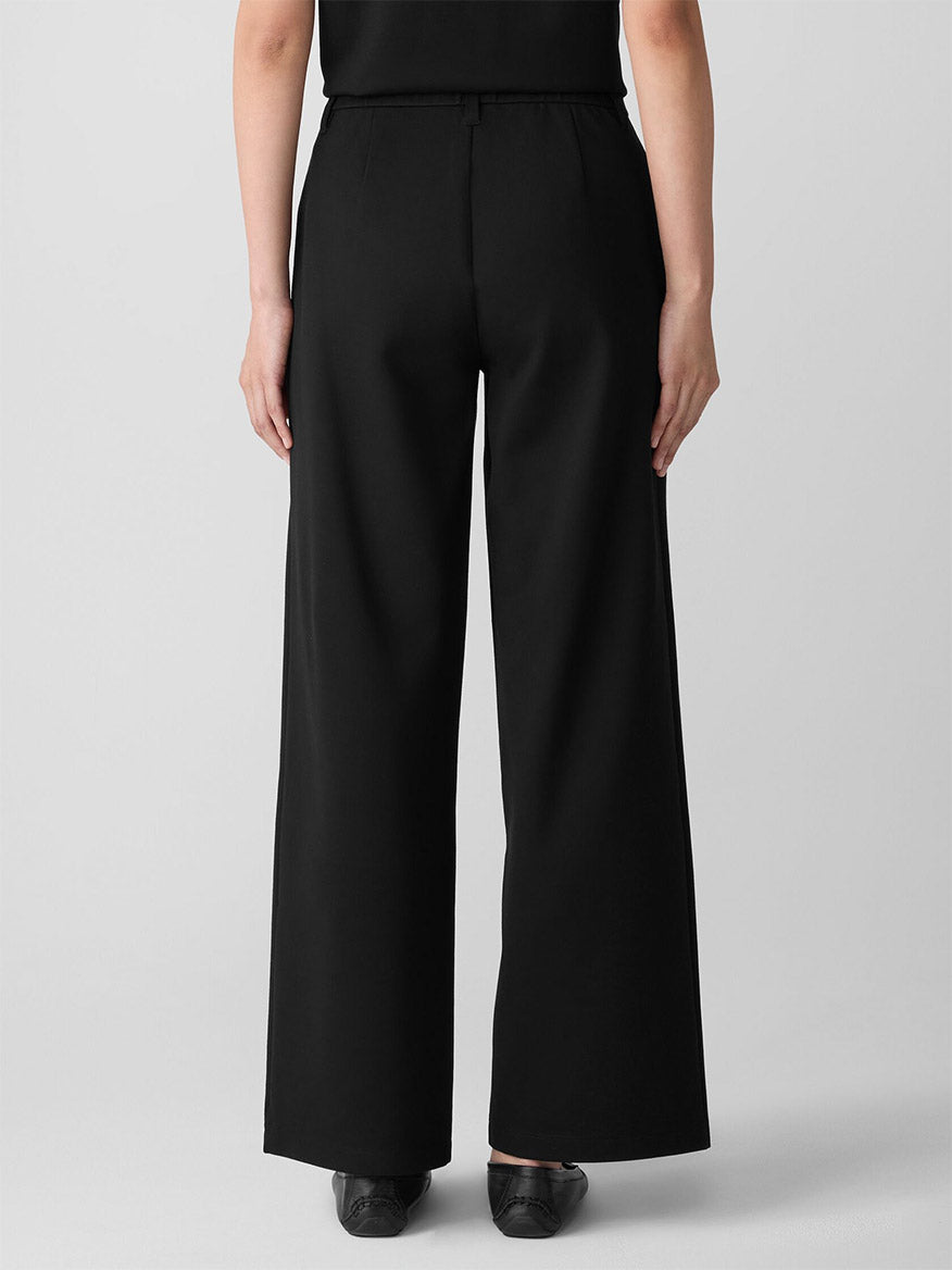 A person faces away, wearing the Eileen Fisher Washable Flex Ponte Wide Trouser Pant in Black and black shoes, set against a plain light gray background.