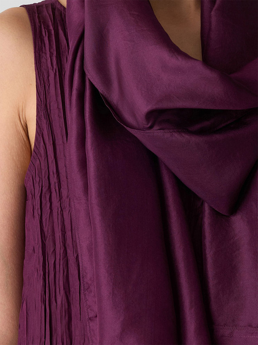 Close-up of a person in a sleeveless textured purple top, draped with the Eileen Fisher Washed Transitional Silk Scarf in Blackberry, showing only part of their upper body.