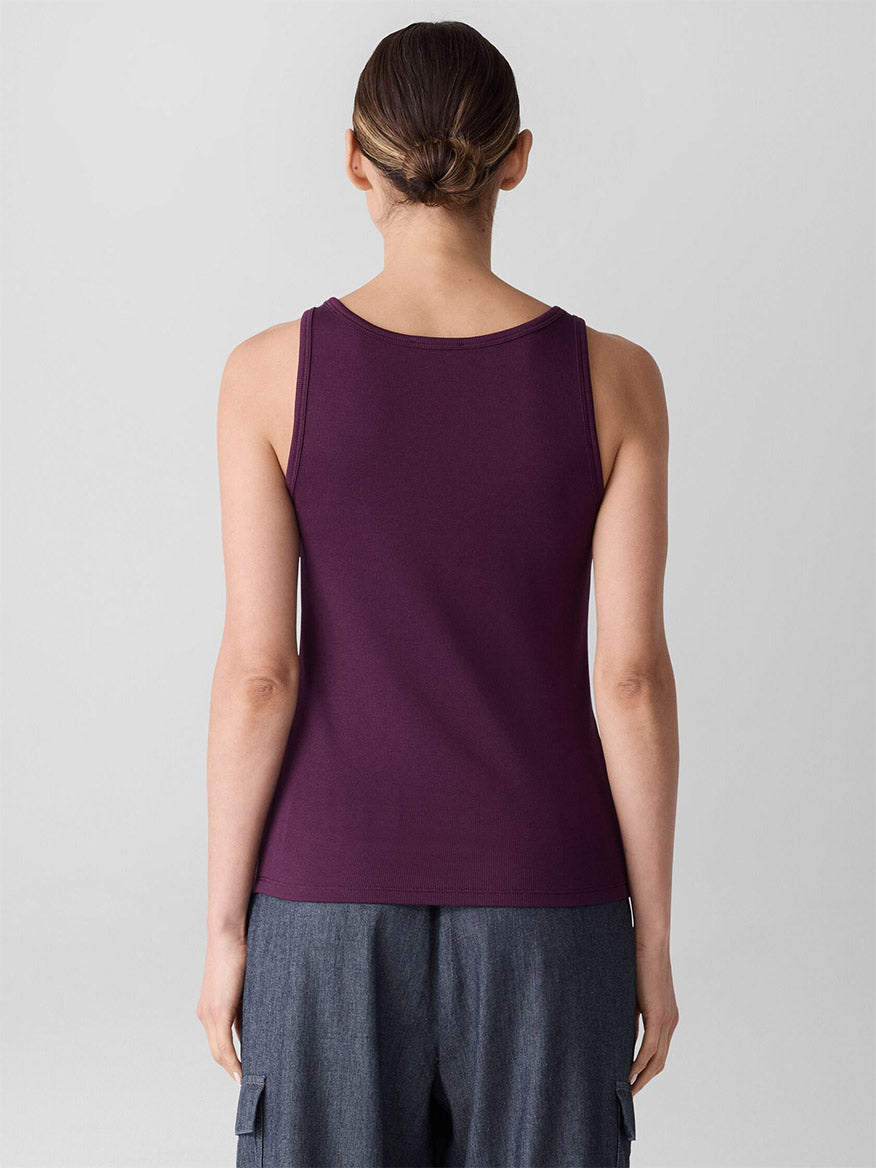 A woman faces away from the camera wearing the Eileen Fisher Organic Cotton Stretch Rib Scoop Neck Tank in Blackberry and gray ribbed pants, set against a plain light background.