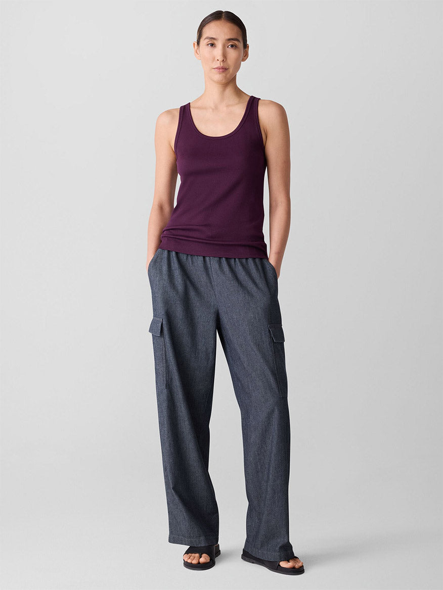 A woman faces forward, wearing the Eileen Fisher Organic Cotton Stretch Rib Scoop Neck Tank in Blackberry and loose gray cargo pants, hands in her pockets against a plain background.