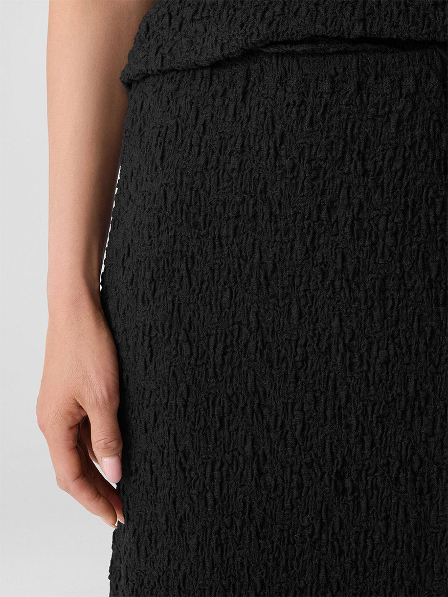 A close-up of a person wearing the Eileen Fisher Bubble Jacquard Pencil Skirt in Black, featuring a textured cotton blend, with their left hand resting by their side.