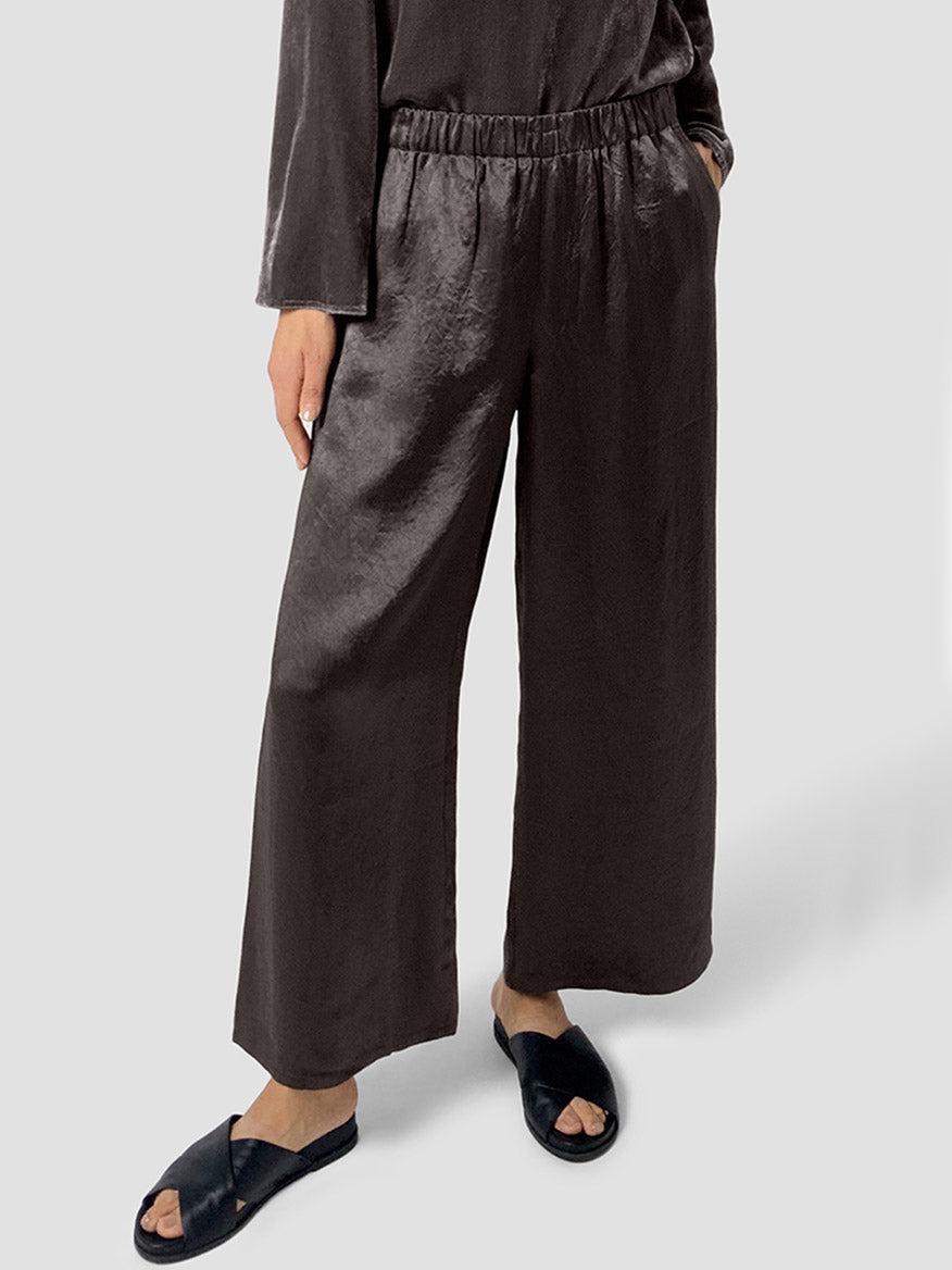 Person wearing the Eileen Fisher Textured Satin Wide-Leg Pant in Rye with a matching long-sleeve top and black open-toe slide sandals, standing against a light gray background.