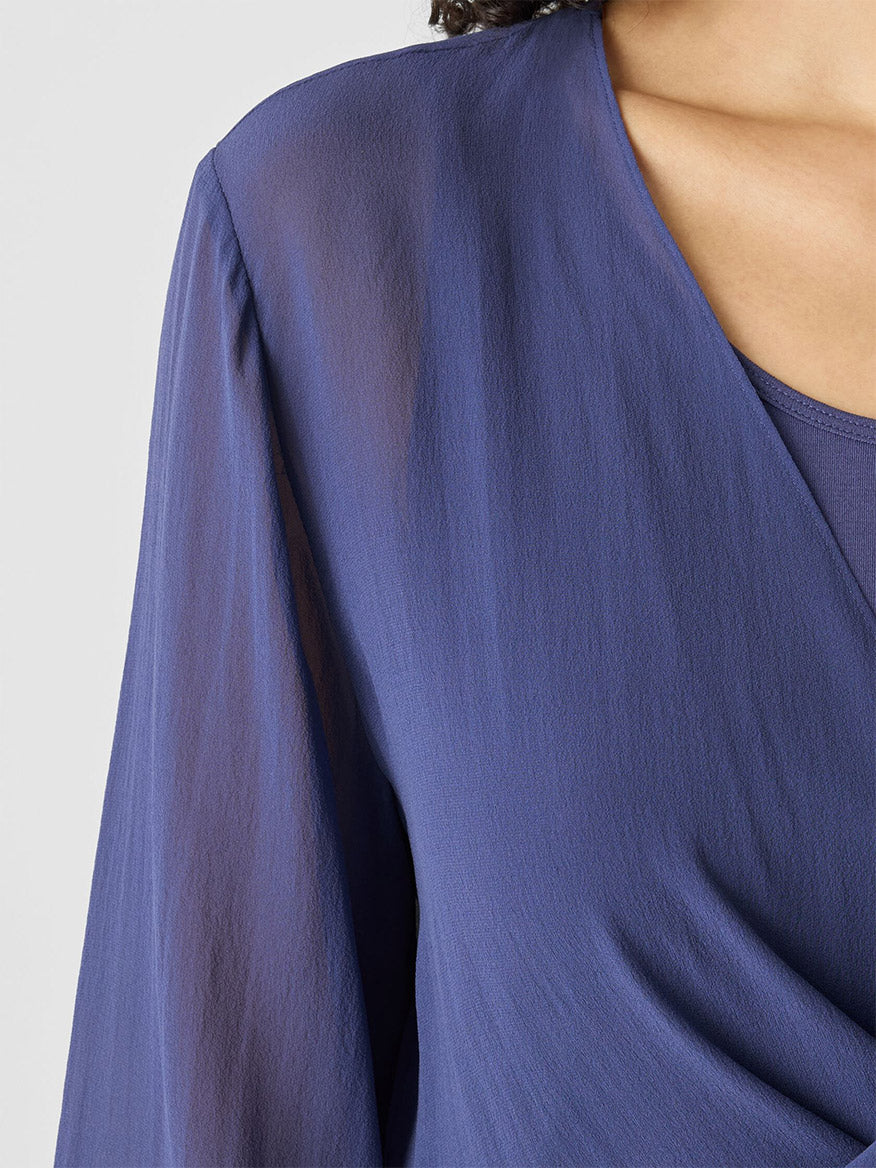 A close-up of a person wearing the Eileen Fisher Sheer Silk Georgette Tie Jacket in Bluette, showcasing blue sheer sleeves and a matching inner garment as the ultimate layering piece.