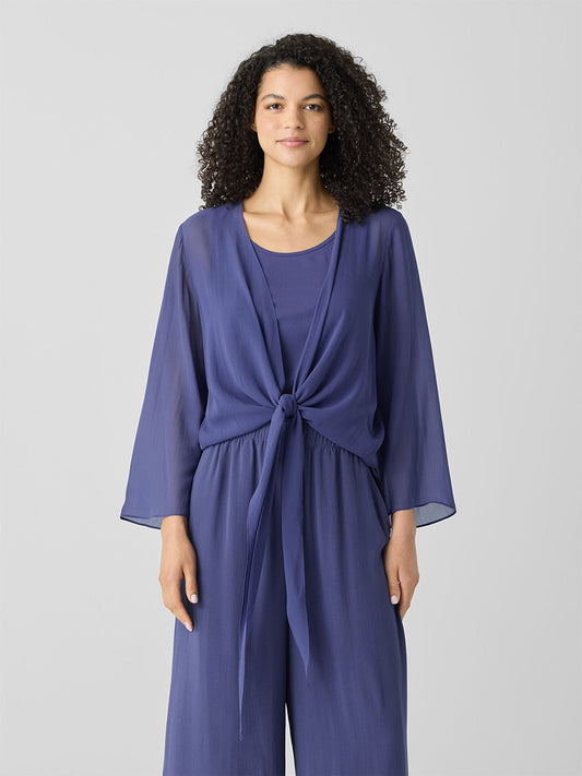 A person wearing the Eileen Fisher Sheer Silk Georgette Tie Jacket in Bluette stands against a plain background. It features cascading ties, three-quarter sleeves, and a chic tie-front design, making it the ultimate layering piece.
