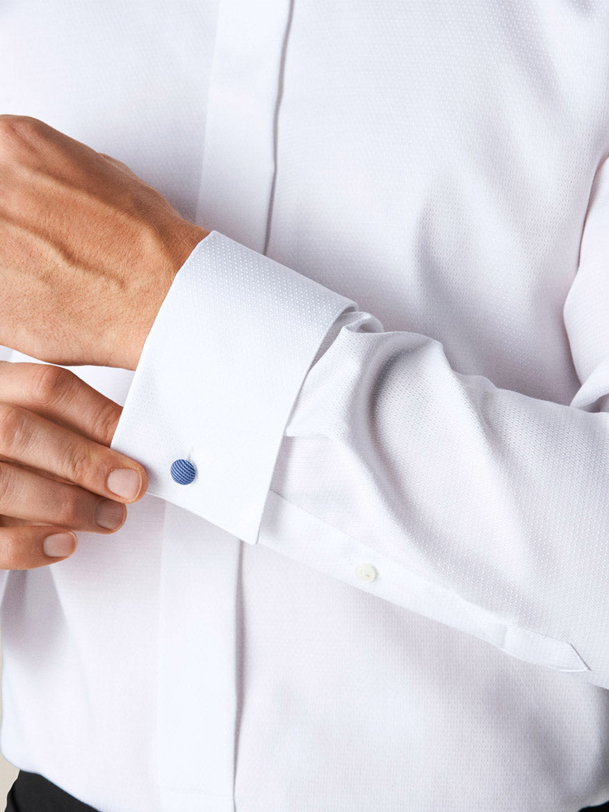 A person adjusts the cufflink on the sleeve of an Eton White Dobby Formal Shirt made from dobby fabric with a subtle textured pattern.
