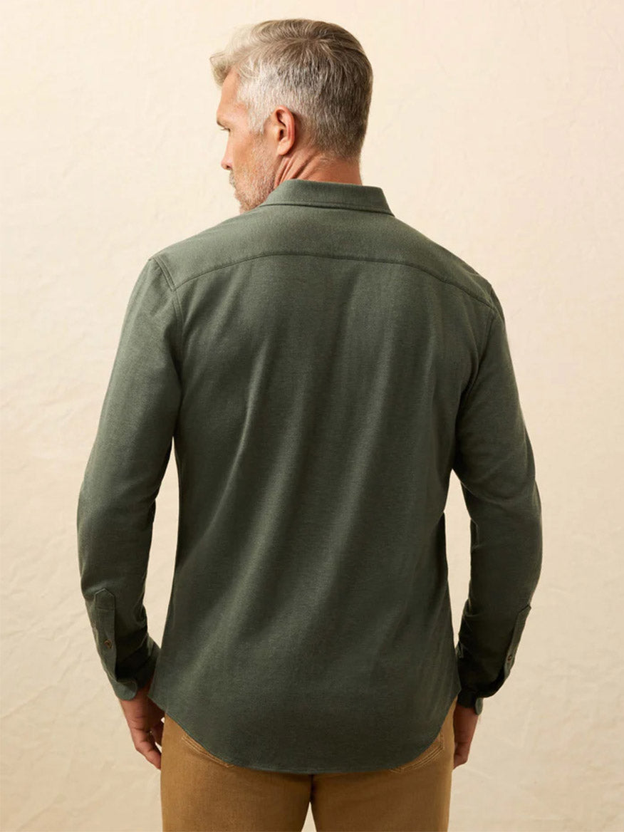 A man with short gray hair, seen from the back, wears the Faherty Brand Coastline Knit Shirt in Forest Heather Twill and tan pants against a neutral background.