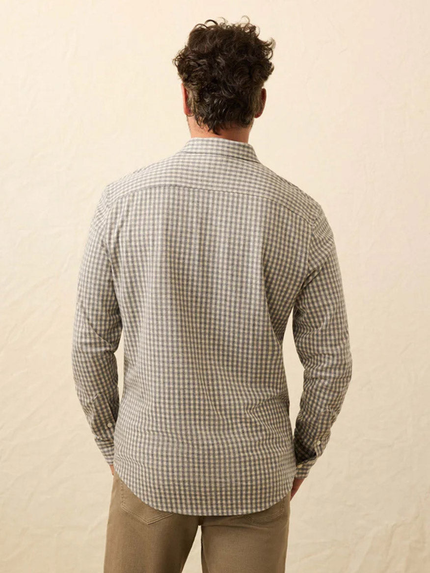 A man faces away from the camera, wearing the Faherty Brand Coastline Knit Shirt in Fox Grey Gingham with light brown pants against a neutral background.