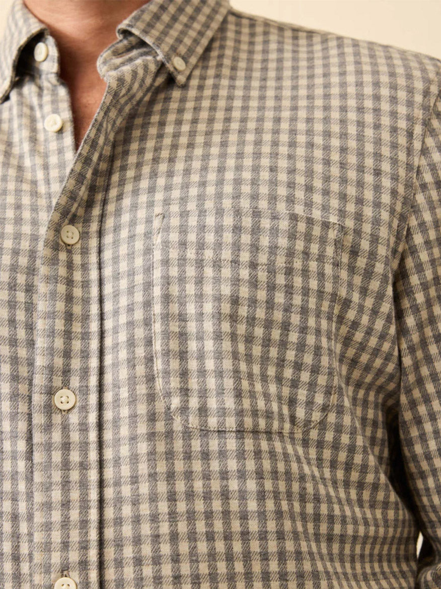 Close-up of a person wearing the Faherty Brand Coastline Knit Shirt in Fox Grey Gingham, a comfortable stretch shirt with grey and white checks, chest pocket, and light-colored buttons.