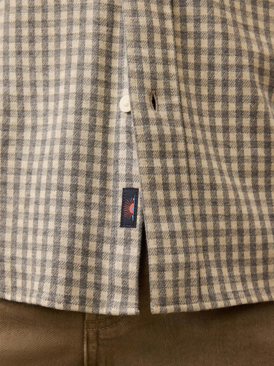 Close-up of the Faherty Brand Coastline Knit Shirt in Fox Grey Gingham—a versatile button-down with a small logo tag by the hem, styled over brown pants.