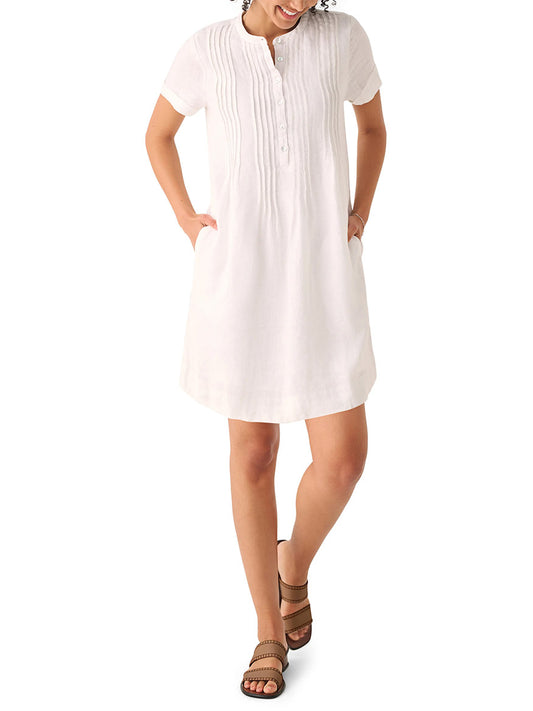 A woman in a Faherty Brand Gemina Basketweave Dress in White and brown sandals stands smiling, her hands slightly behind her.