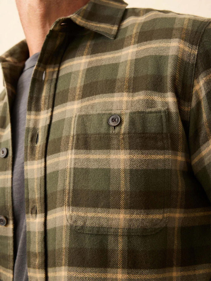 Close-up of a person wearing the Faherty Brand Heirloom Portuguese Flannel Shirt in Garrett Verde Plaid over a gray t-shirt, highlighting its chest pocket and button details.
