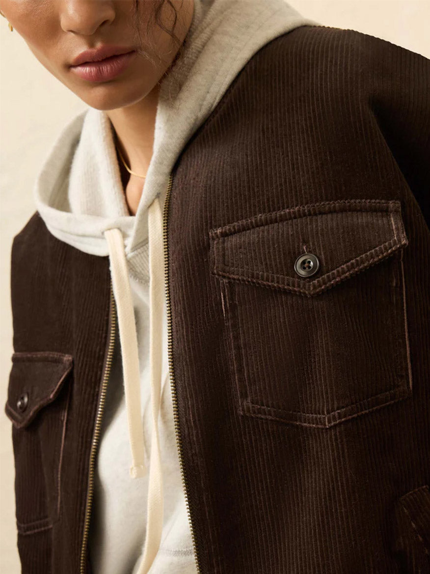 A person wearing a white hoodie under the Faherty Brand Heritage Cord Jacket in Chocolate Brown, featuring front flap pockets and a zipper—perfect for casual fall style.