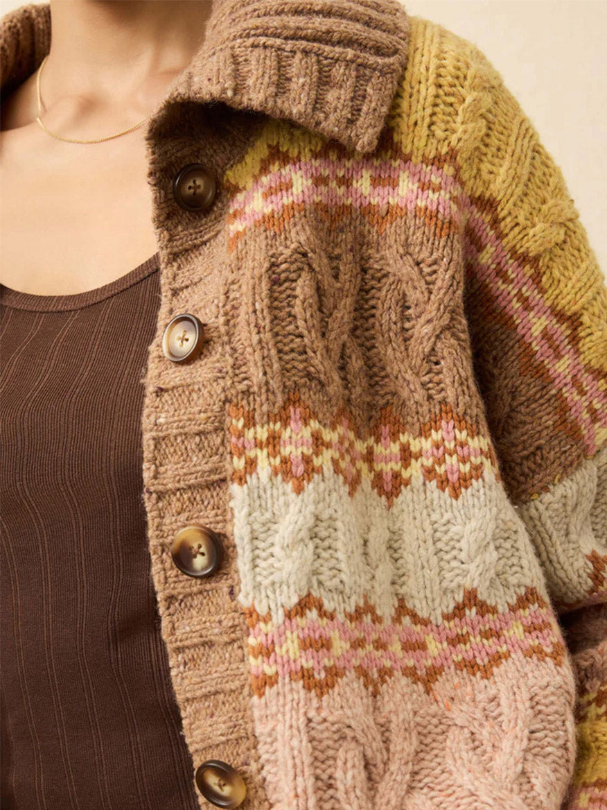 Close-up of a person wearing the Faherty Brand Highland Fairisle Cardigan in Lakeside Fairisle Haze, featuring chunky cable knit, large buttons, and festive multicolored stripes—perfect for cozy winter days.