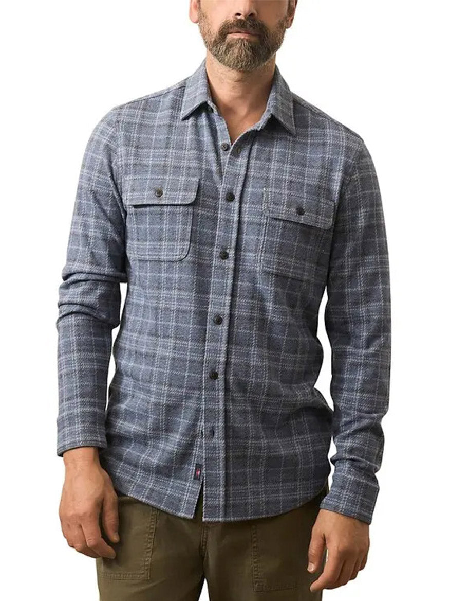 A man stands against a white background wearing the Faherty Brand Legend Sweater Shirt in Castle Lake Plaid, which features blue and gray checks and two chest pockets.