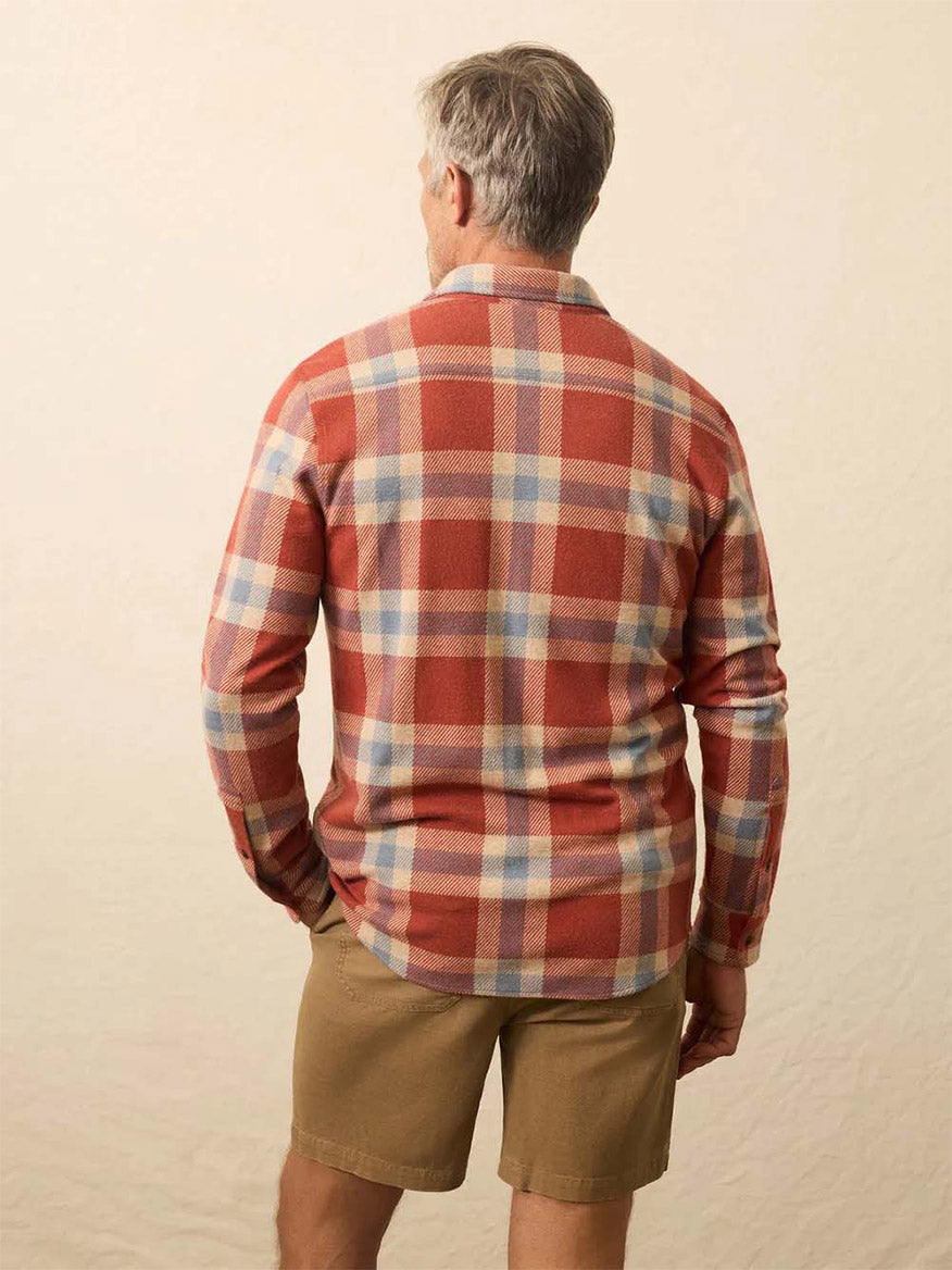 A man with gray hair is standing facing away, wearing a Faherty Brand Legend Sweater Shirt in Copper Falls Plaid and tan shorts against a neutral background.