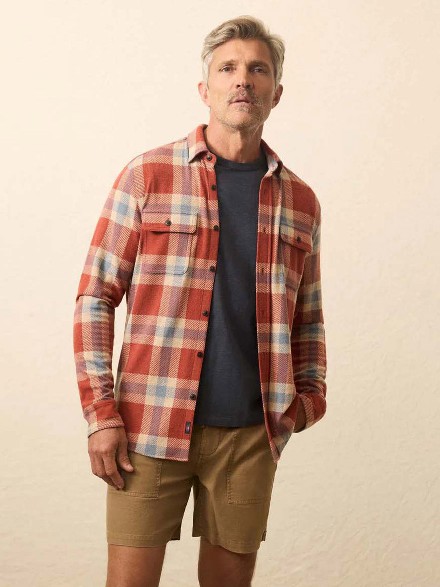 A man faces forward, wearing the Faherty Brand Legend Sweater Shirt in Copper Falls Plaid over a dark t-shirt and khaki shorts, set against a plain background.