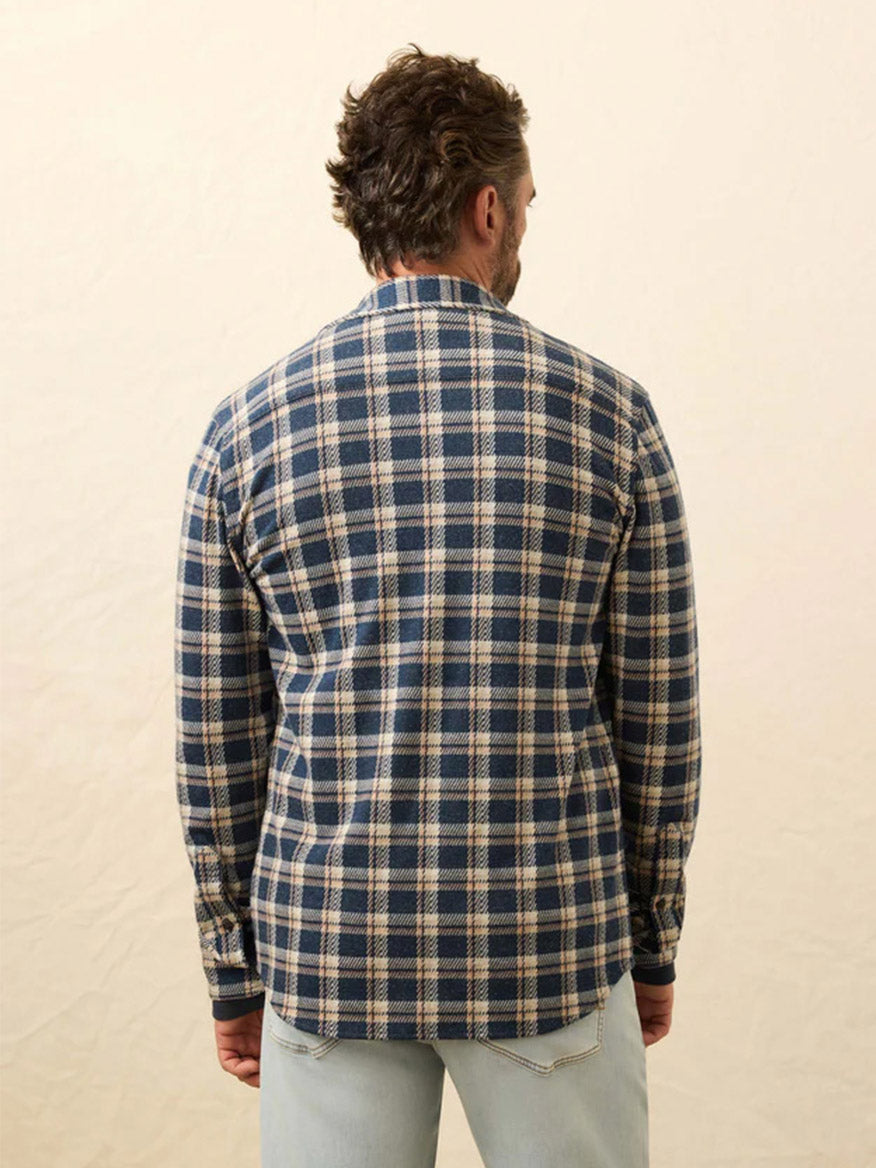 A man faces away from the camera, wearing the Faherty Brand Legend Sweater Shirt in Golden Lake Plaid with light jeans, set against a plain, neutral background.