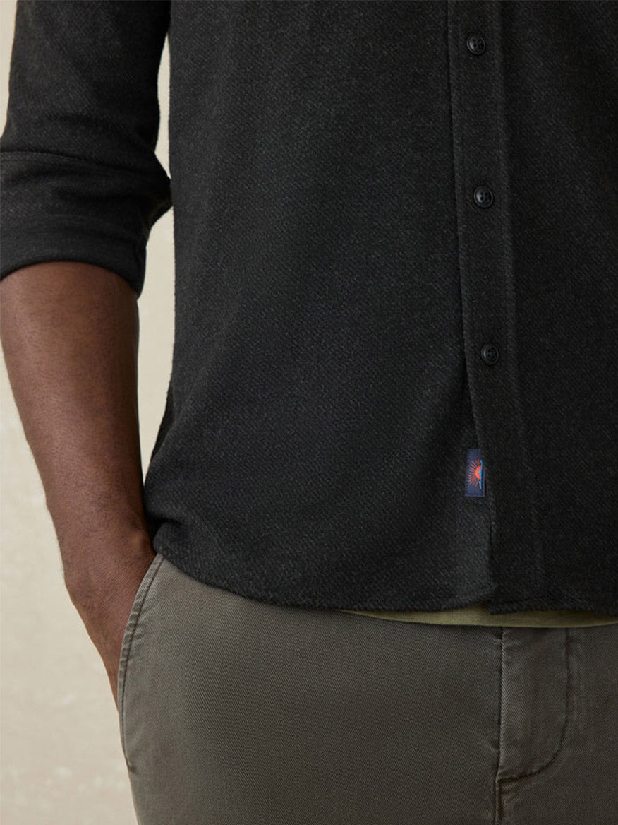 A person wearing the Faherty Brand Legend Sweater Shirt in Heathered Black Twill with sleeves rolled up and light olive pants, one hand in their pocket.