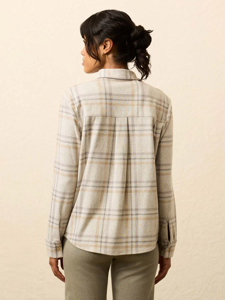 A woman faces away, wearing the Faherty Brand Legend™ Classic Sweater Shirt in Sandy Trails Plaid with light-colored pants against a plain, light background.
