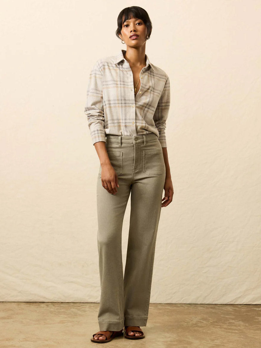 A woman stands against a plain background, wearing the Faherty Brand Legend™ Classic Sweater Shirt in Sandy Trails Plaid, paired with high-waisted beige pants and brown sandals.