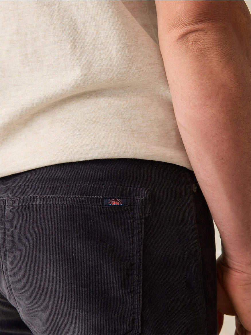 Close-up of a person wearing a beige shirt and the Faherty Brand Stretch Terry Corduroy 5-Pocket Pant in Washed Charcoal, featuring a classic fit and a small logo on the back pocket.
