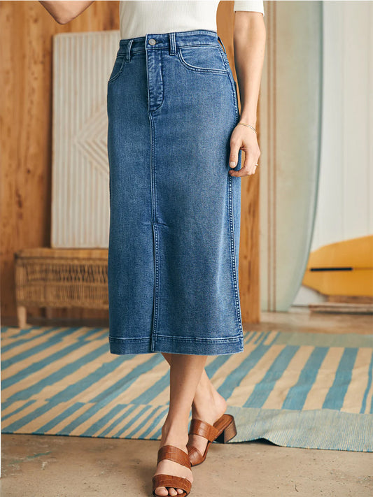 A person standing in a room wearing a white top, the Faherty Brand Stretch Terry Midi Skirt in Riverton Wash, and brown sandals.