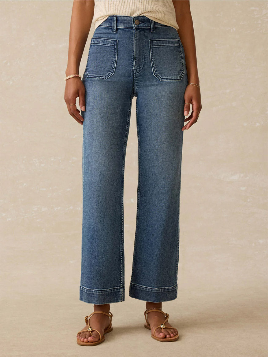 Wearing Faherty Brand Stretch Terry 5-Pocket Ankle Pant in Riverton, a sleeveless relaxed-fit ribbed top, sandals, and a bracelet, a person stands against a plain background.