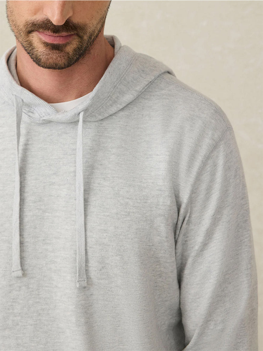A man with a short beard models the Faherty Brand Sunwashed Midweight Organic Hoodie in Light Grey Heather, worn relaxed over a white shirt and shown from the shoulders up against a neutral background.