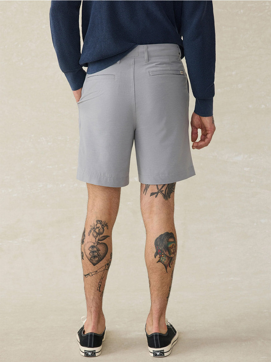 A person is shown from the back wearing Faherty Brand All Day Short in Ice Grey, a navy long-sleeve shirt, and black sneakers, revealing leg tattoos. The water-repellent fabric adds versatility to this stylish outfit.